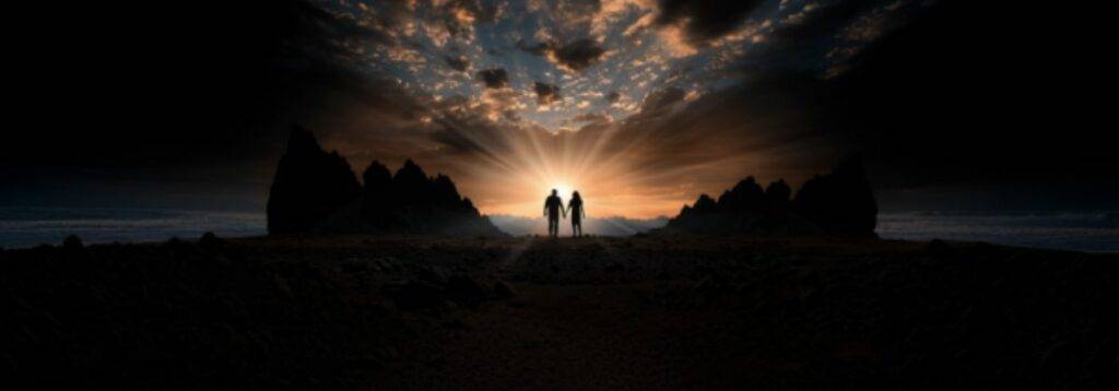 Two figures, silhouetted against a dramatic sunrise, walk hand in hand through a rugged landscape toward the horizon, symbolizing unity, hope, and purpose.